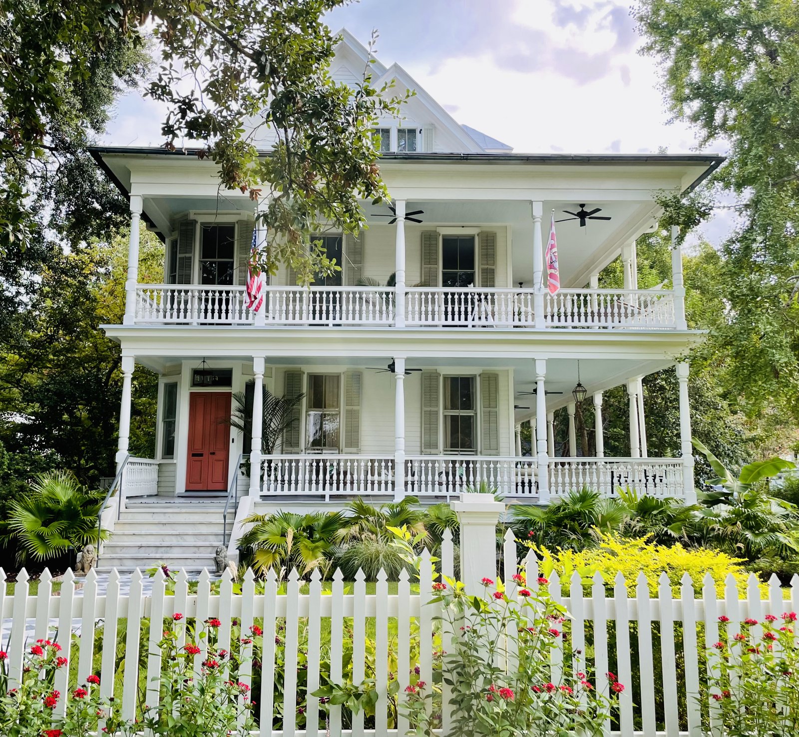 White two-story Charleston home with double porches, a red front door and a picket fence