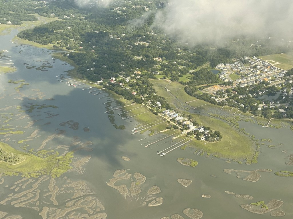 Aerial view of docks reaching into a tidal creek, with marsh and neighborhoods beyond
